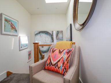 A small seating area with a beige armchair a colorful pillow a yellow throw and framed bird artwork on walls at Stargazers in Sennen