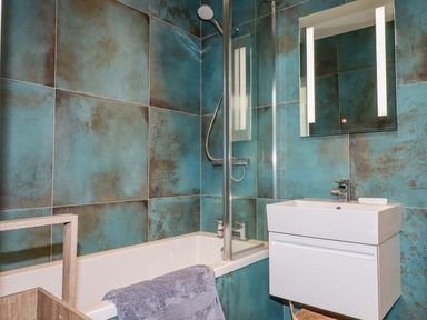 A bathroom with a bathtub shower combination a sink with a faucet and a mirror at Stargazers in Sennen