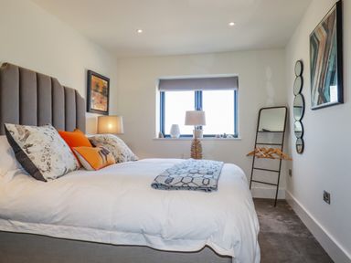 A bedroom with a bed a window two lamps a mirror with hangers and wall art at Stargazers in Sennen