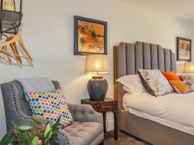 A bedroom with a bed with pillows a bedside table with a lamp an armchair with a cushion hangers on a wall rack and framed pictures at Stargazers in Sennen