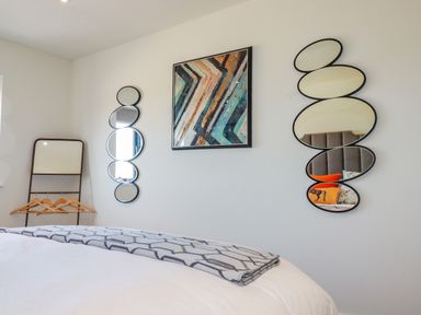 A bedroom wall with two sets of oval mirrors a framed abstract painting and a standing mirror with hangers at Stargazers in Sennen