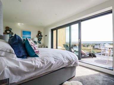 A bedroom with a bed with pillows near glass sliding doors opening to a balcony with chairs at Stargazers in Sennen