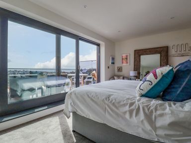 A bedroom with a bed pillows mirror table lamp and balcony doors at Stargazers in Sennen