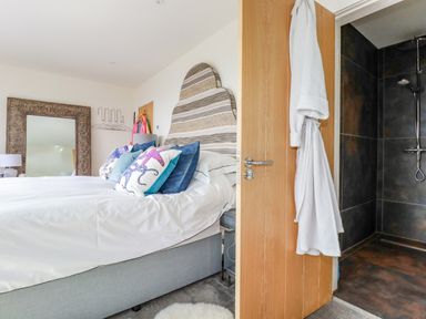 A bedroom with a bed with patterned pillows a decorative mirror and an open door showing a shower at Stargazers in Sennen