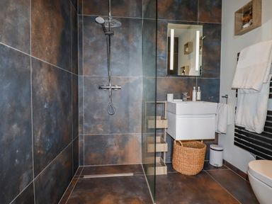 A bathroom with dark tiles a glass shower enclosure a white floating sink a mirror and towels at Stargazers in Sennen