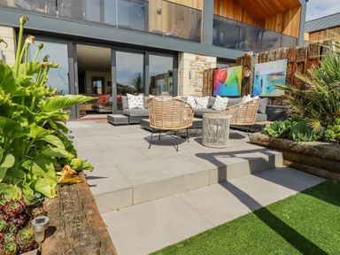 An outdoor patio with chairs sofa table plants and abstract paintings at Stargazers in Sennen