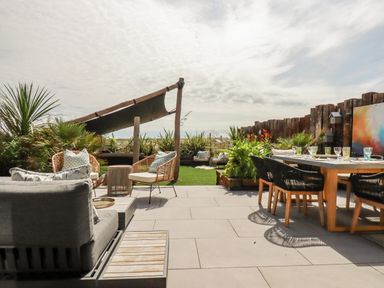 An outdoor patio with dining table chairs lounge seating plants and a shade sail at Stargazers in Sennen