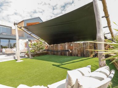 An outdoor patio area with a black shade sail a hammock artificial grass and outdoor seating at Stargazers in Sennen