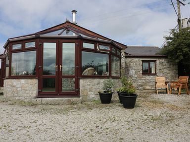 A stone house with a glass conservatory and wooden chairs outside at Sheilas Cottage in Penryn
