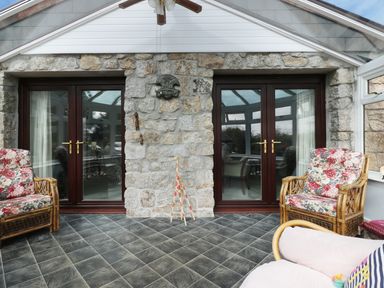 A conservatory with tiled floor wicker chairs with floral cushions and double glass doors