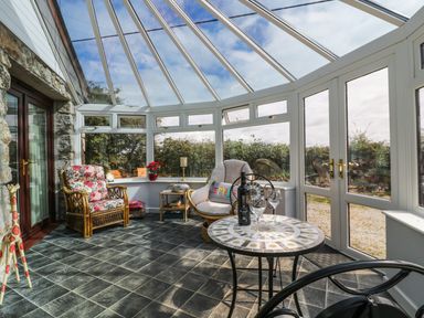 A conservatory with wicker chairs a small table with wine bottle and glasses and tiled floor at Sheilas Cottage in Penryn