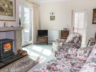 A living room with floral upholstered sofa and armchair a wood burning stove and a small television at Sheilas Cottage in Penryn
