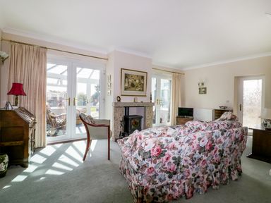 A living room with floral sofa a fireplace and glass doors at Sheilas Cottage in Penryn