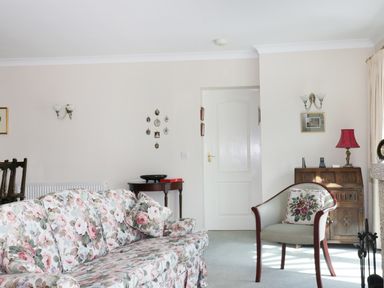 A living room with floral sofa, armchair, small wooden tables, lamps, and framed pictures at Sheilas Cottage in Penryn