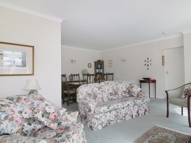 A living room with floral sofas a dining table with chairs a bookcase and framed pictures at Sheilas Cottage in Penryn