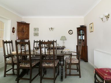 A dining room with a wooden table and chairs a wooden cabinet and bookshelf with a lamp and wall decorations at Sheilas Cottage in Penryn