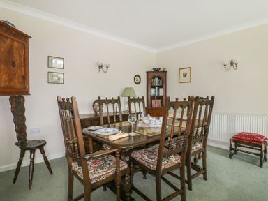 A dining room with a wooden table and six chairs with floral cushions at Sheilas Cottage in Penryn