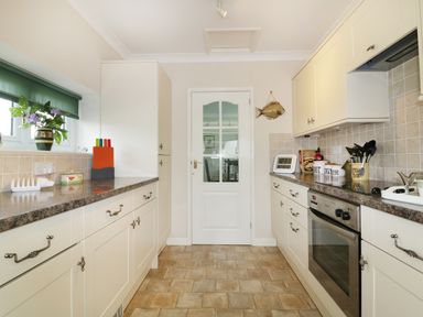 A galley kitchen with white cabinets countertop appliances and a door at Sheila's Cottage in Penryn