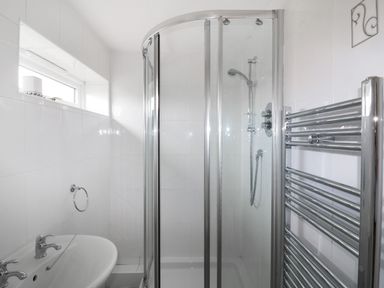 A bathroom with a shower enclosure a sink a towel rack and a small window at Sheilas Cottage in Penryn