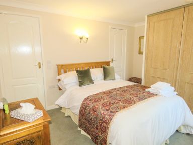 A bedroom with a bed with pillows and a patterned runner next to a wooden bedside table with tissues at Sheila's Cottage in Penryn