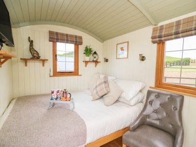 A bedroom with a bed set with pillows and a tray of drinks and croissants and a chair near windows at Ivy's Way in Rhayader