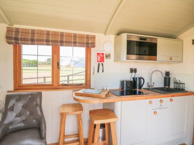 A kitchen area with stools a window and appliances at Ivys Way in Rhayader
