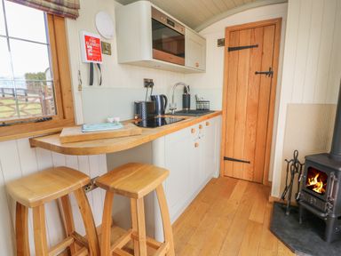 A small kitchen with wooden stools wooden countertop stove and wood burning stove at Ivys Way in Rhayader