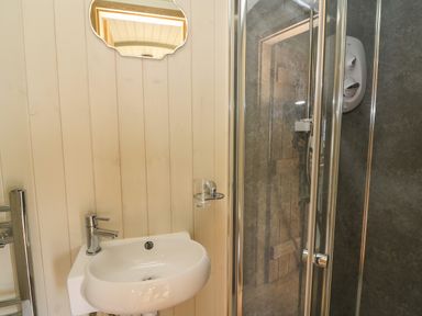 A bathroom with a wall-mounted sink a small mirror a glass holder and a shower with glass doors at Ivys Way in Rhayader