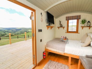 A bedroom with a bed, shelves, TV, and an open door to a deck with a view of hills at Ivys Way in Rhayader