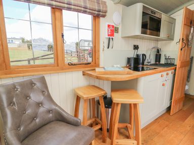 A small kitchen with stools a leather chair and a window showing outside at Ivys Way in Rhayader