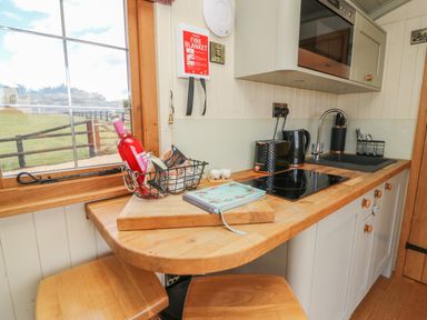 A kitchen countertop with a cutting board, a basket holding a bottle and snacks, a cookbook, toaster, kettle, stovetop, sink, and utensils at Ivys Way in Rhayader