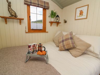 A bedroom with a bed holding pillows and a tray with croissants and cups by a window at Ivys Way in Rhayader