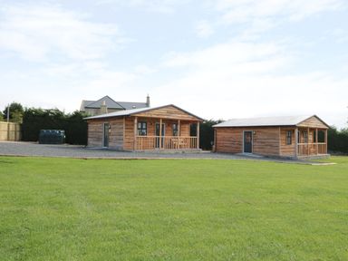 Two wooden cabins with small porches on a gravel area and green grass in front at Aln in Longframlington