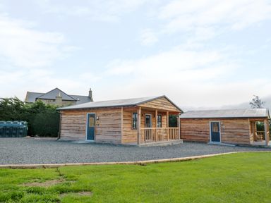 Two wooden cabins with blue doors on a gravel area next to a green lawn at Aln in Longframlington