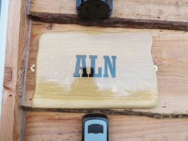 A wooden plaque with the letters ALN mounted on a wooden wall with a doorbell below at Aln in Longframlington