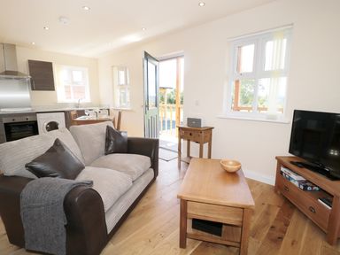 A living room with a sofa coffee table television and kitchen area visible at Aln in Longframlington