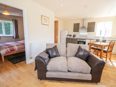 A living area with a two-seater sofa and an open kitchen with a dining table and chairs at Aln in Longframlington
