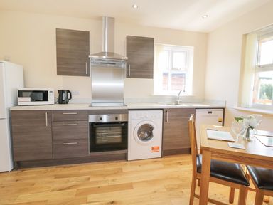 A kitchen with wooden cabinets a washing machine an oven microwave and dining table at Aln in Longframlington
