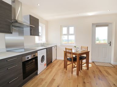 A kitchen with wooden cabinets washing machine oven and a small dining table with two chairs at Aln in Longframlington