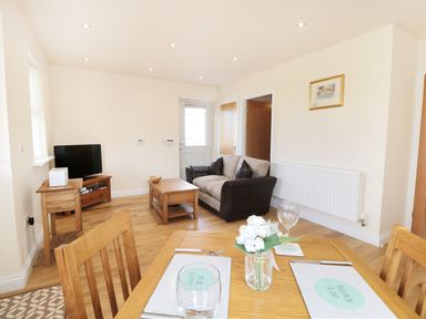 A living room and dining area with wooden furniture a sofa a television and a door at Aln Longframlington