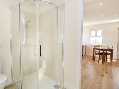A bathroom with a glass shower enclosure and a view of a dining area with a wooden table and chairs at Aln in Longframlington