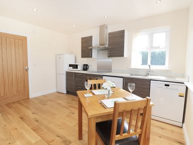 A kitchen with wooden floor cabinets a wooden dining table with two chairs and kitchen appliances at Aln in Longframlington