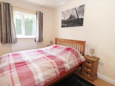 A bedroom with a wooden bed and nightstand with a lamp under a window with curtains at Aln in Longframlington
