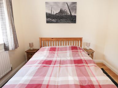 A bedroom with a wooden bed frame and red plaid bedding with bedside tables and lamps at Aln in Longframlington