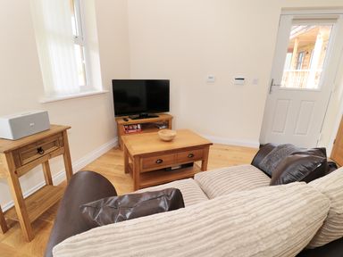 A living room with a couch a wooden coffee table a television on a wooden stand and a side table at Breamish in Longframlington