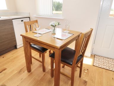 A small dining table with two chairs set with placemats and wine glasses in a kitchen at Breamish in Longframlington