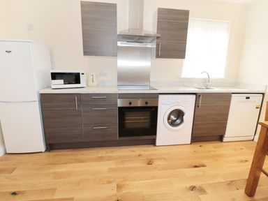 A kitchen with wooden cabinets a refrigerator microwave kettle oven washing machine dishwasher and a sink at Breamish in Longframlington