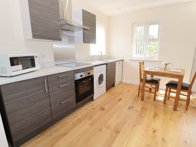 A kitchen with wooden floor cabinets microwave oven washing machine dining table and chairs by the window at Breamish in Longframlington