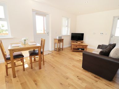 A living area with wooden dining table and chairs a sofa wooden TV stand and side table at Breamish Longframlington