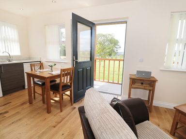 A dining table with two chairs next to an open door leading outside a living space with wooden furniture at Breamish in Longframlington